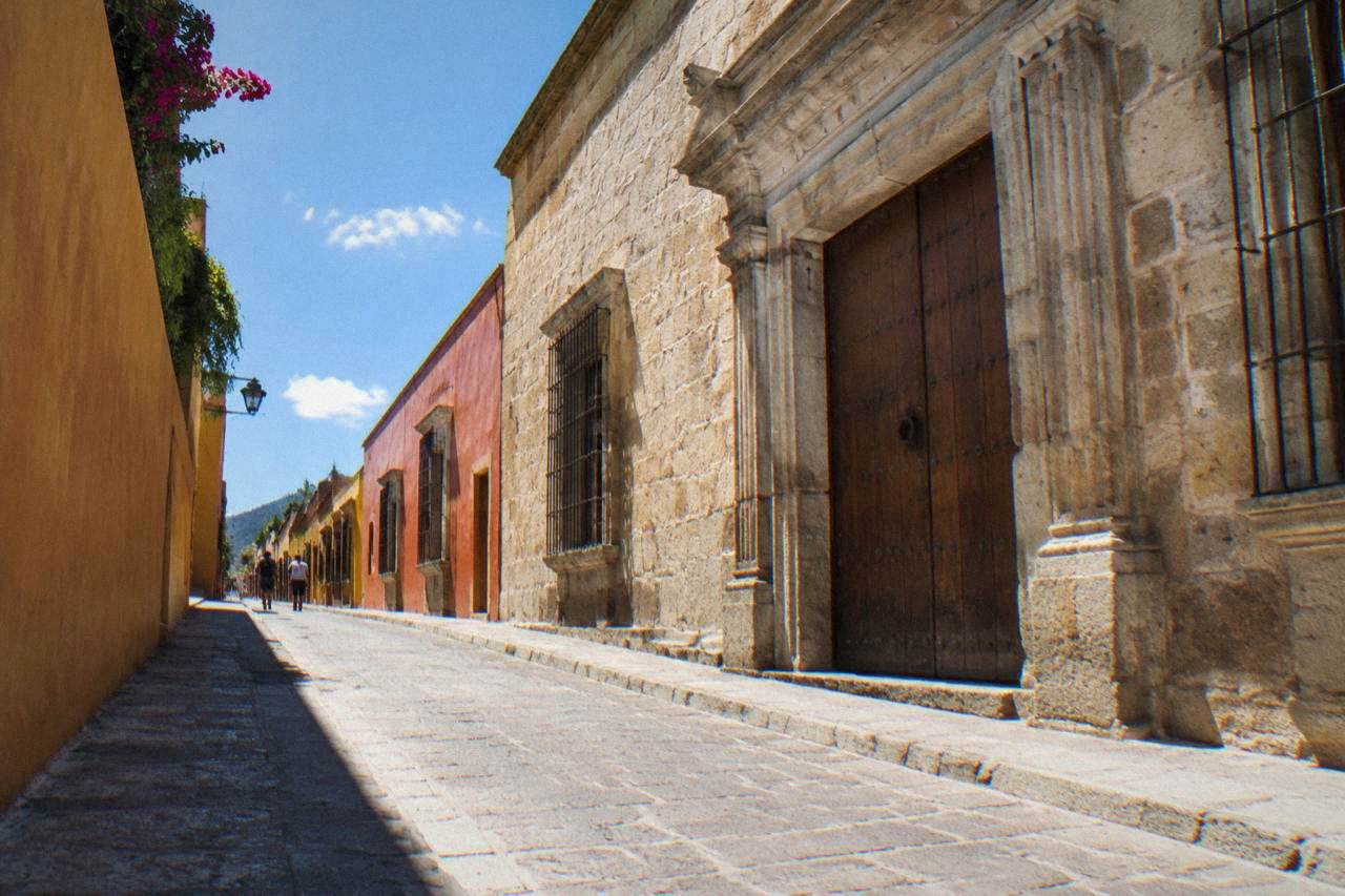 Sunlit colonial street in Oaxaca City with shade cast across a stone facade