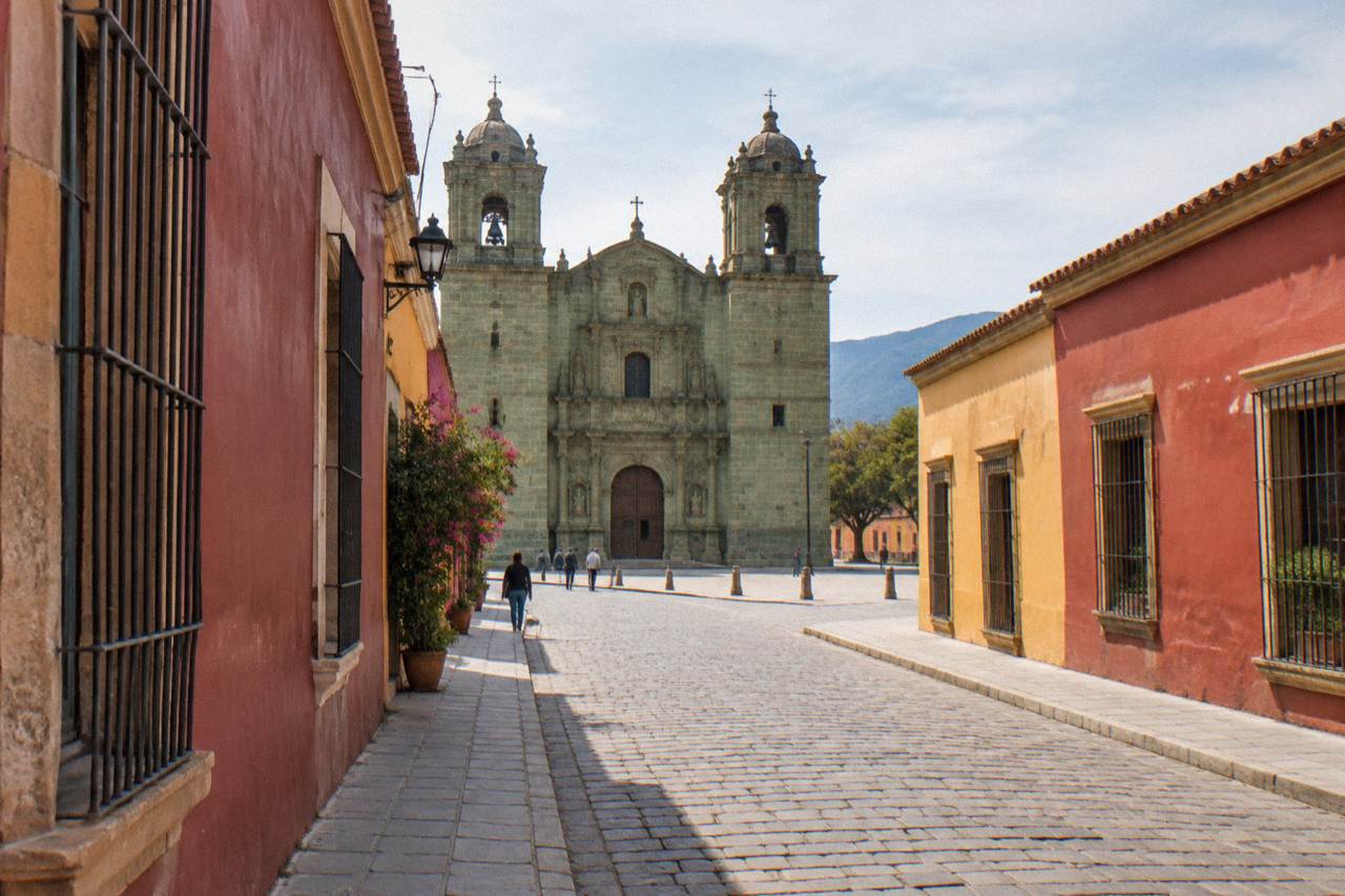 A narrow pedestrian street in Oaxaca City with colourful facades and the church of Santo Domingo ahead