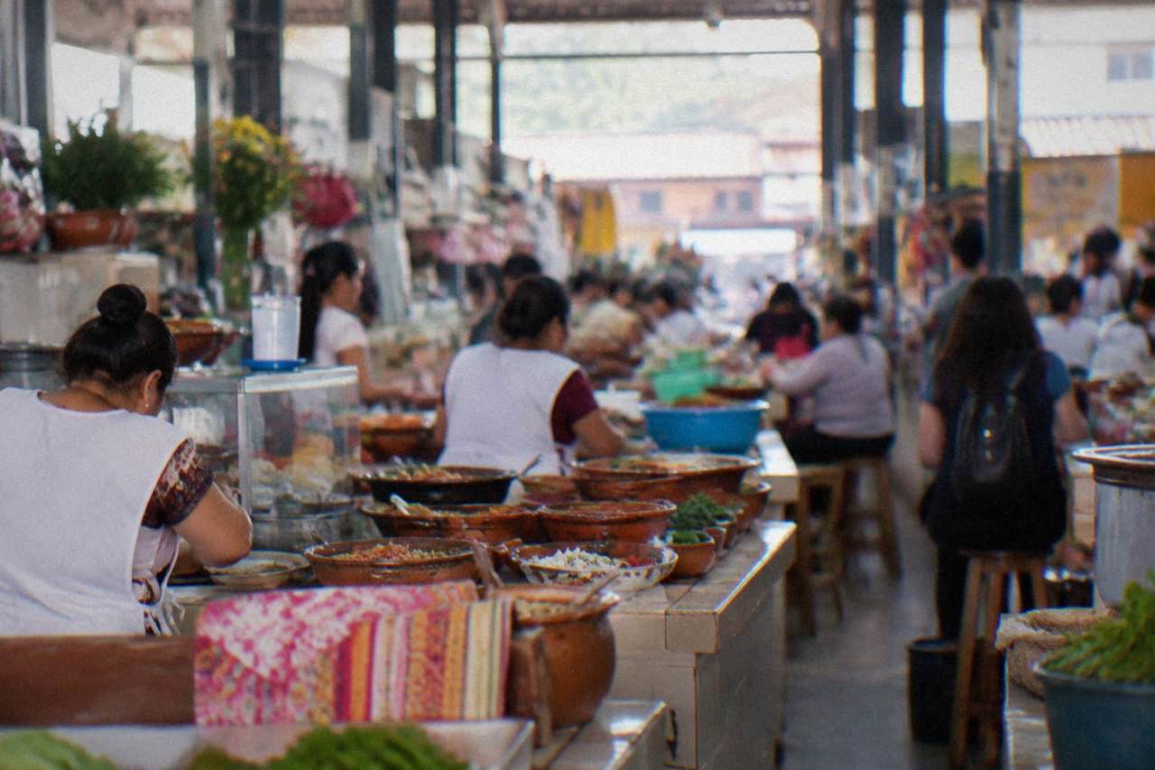 A busy food market hall in Oaxaca City with vendors selling dishes from low counters