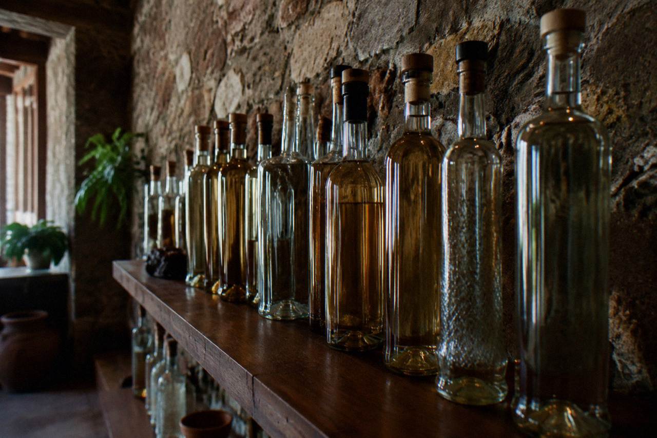 Bottles of mezcal lined up on a wooden shelf in an Oaxaca tasting room