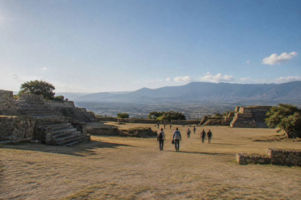 Visitors walking the main plaza of Monte Albán with the Oaxaca valley behind