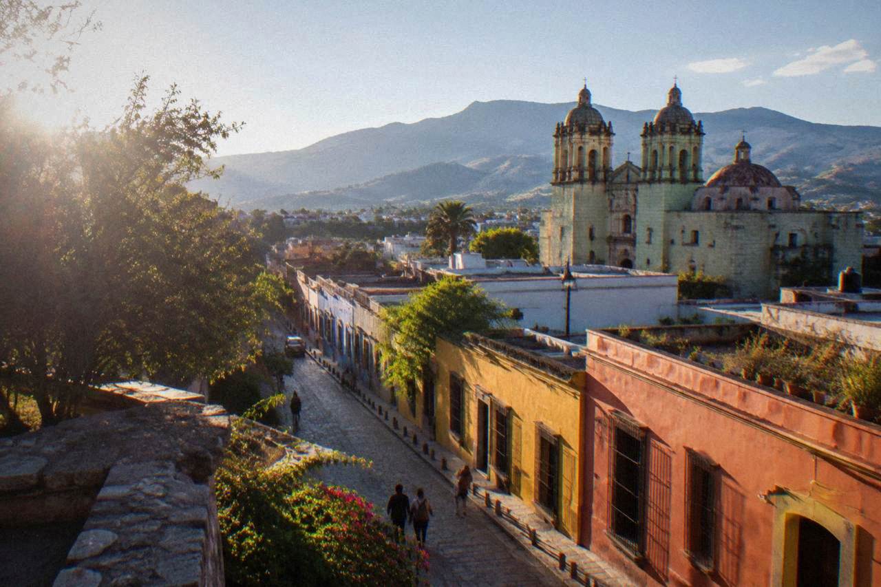 A colonial street in Oaxaca City with coloured facades and a mountain ridge behind