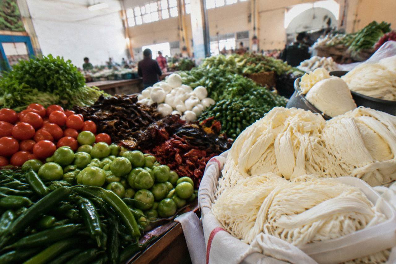 A market stall in Oaxaca with piles of fresh vegetables, chiles and quesillo cheese under warm light