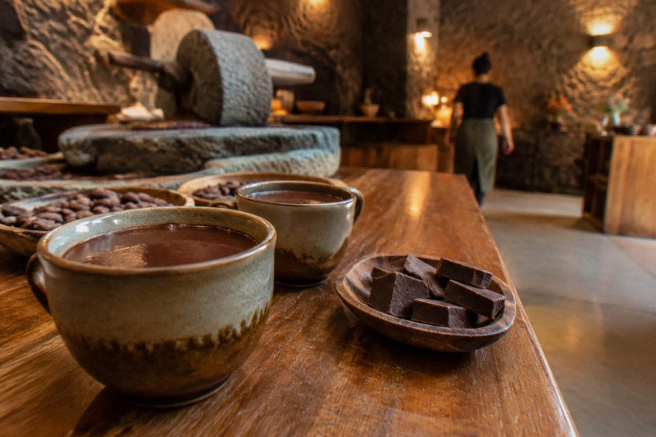 Cups of dark hot chocolate and pieces of chocolate on a wooden counter in Oaxaca