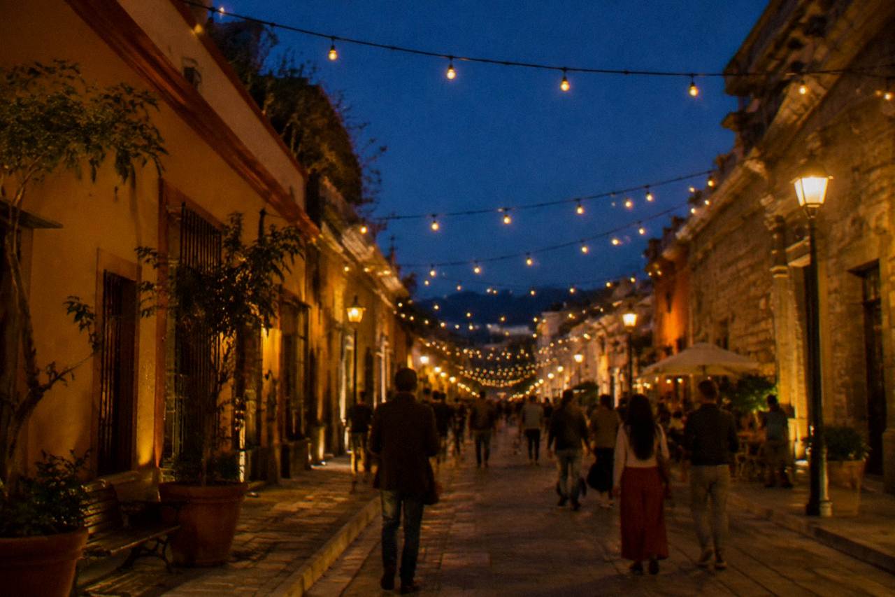 Illuminated colonial street in Oaxaca City at night with people walking under string lights