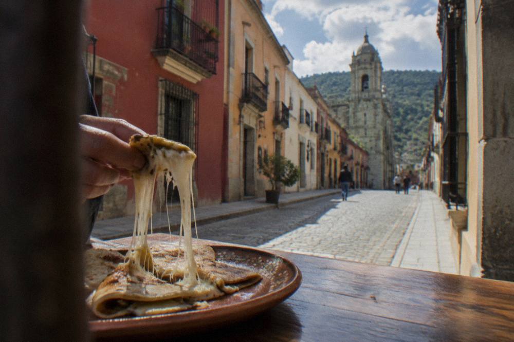 Strings of melted white cheese pulling apart from a hot folded tortilla on a plate