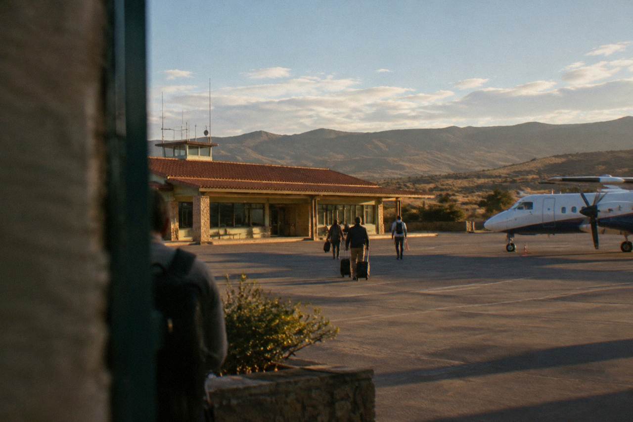 A small regional airport terminal under a wide highland sky, with hills on the horizon