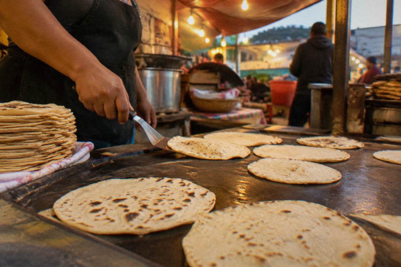 A busy food stall in Oaxaca City grilling large toasted tortillas under warm evening lights