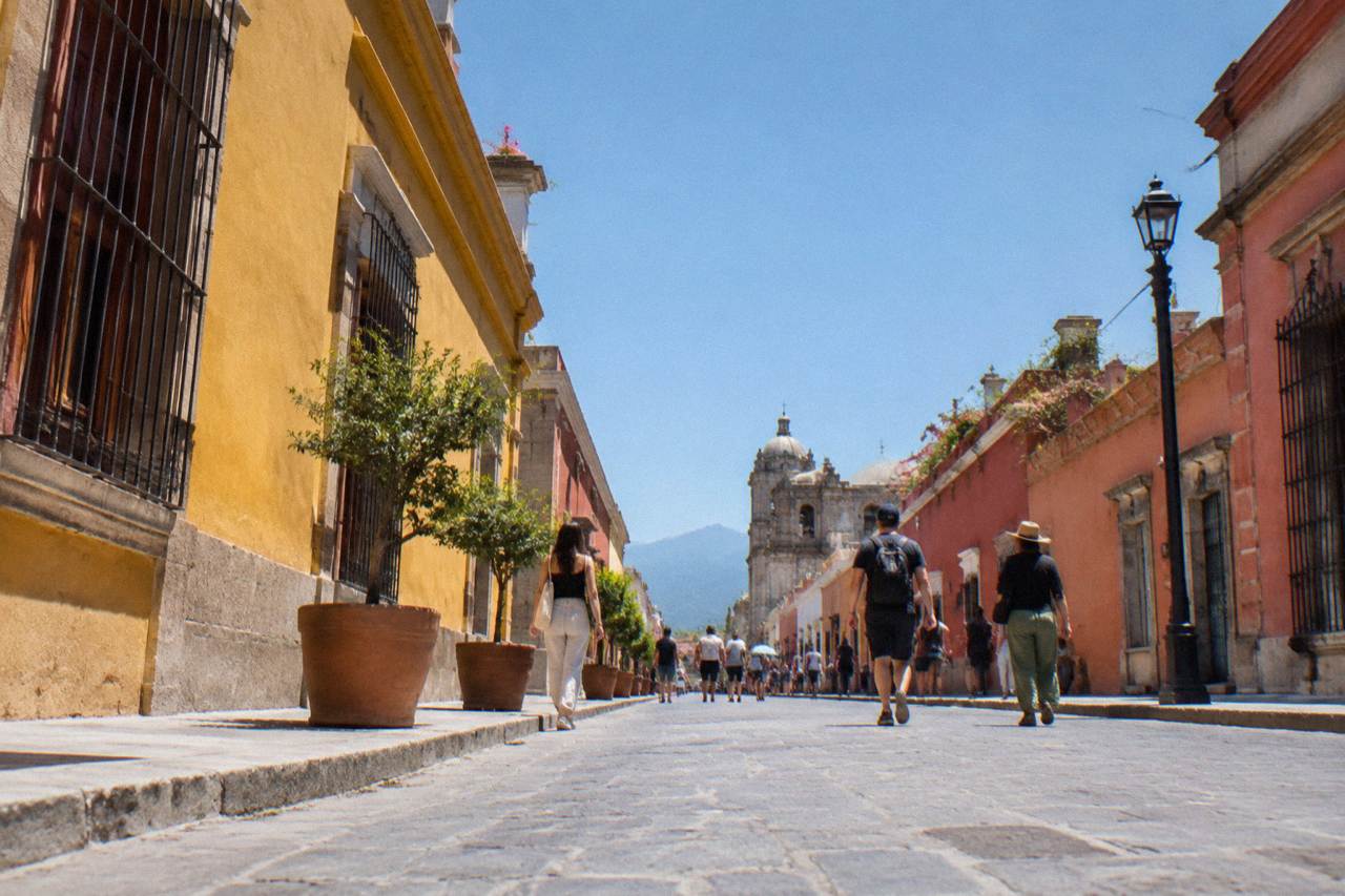 A busy Oaxaca street with colonial buildings in warm colours and people walking under banners