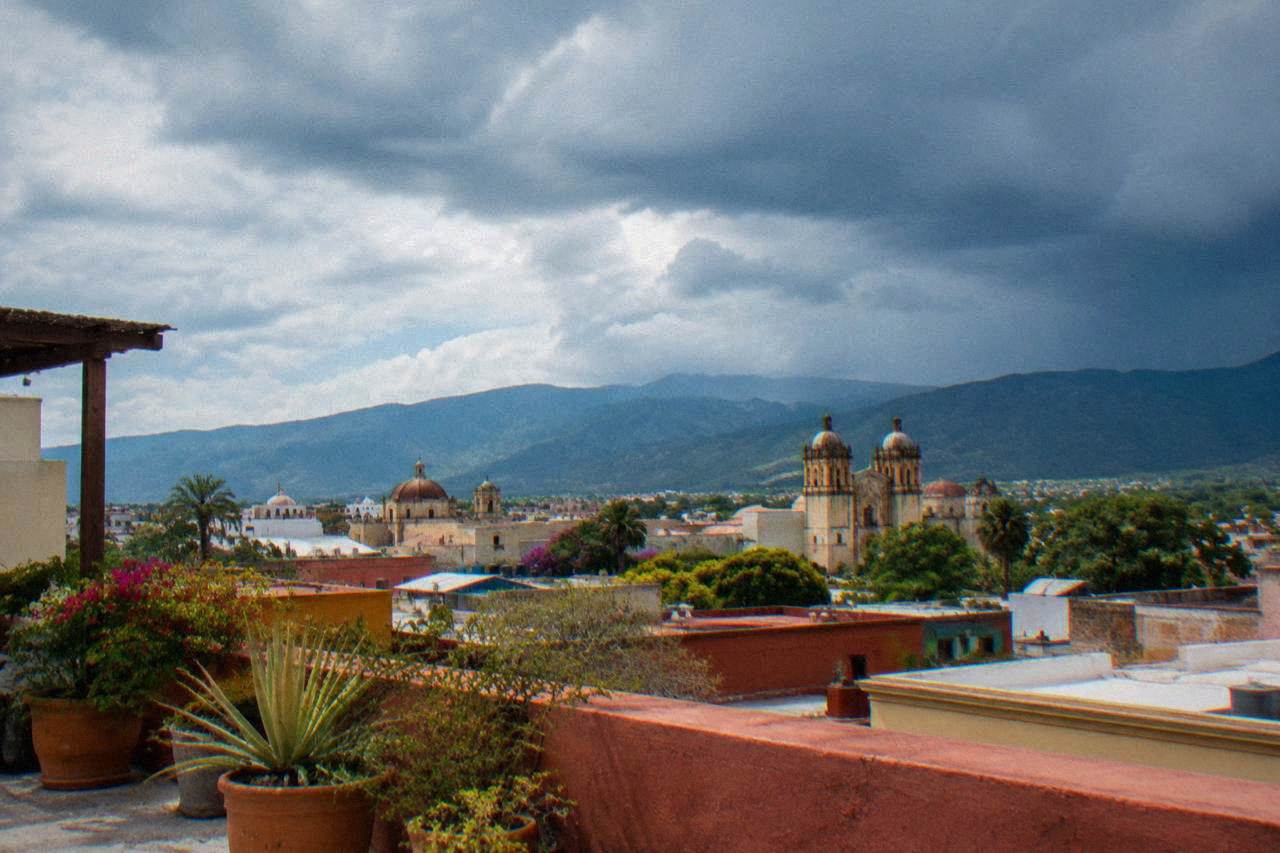 Rain clouds gathering over the rooftops and church domes of Oaxaca City with green hills behind