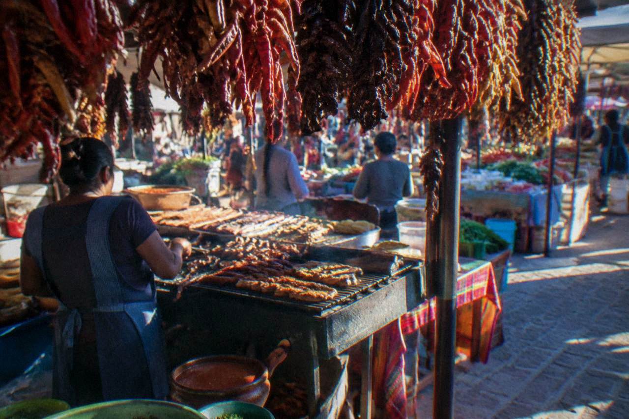 A busy Oaxaca market food stall with grilled meats and hanging dried chiles