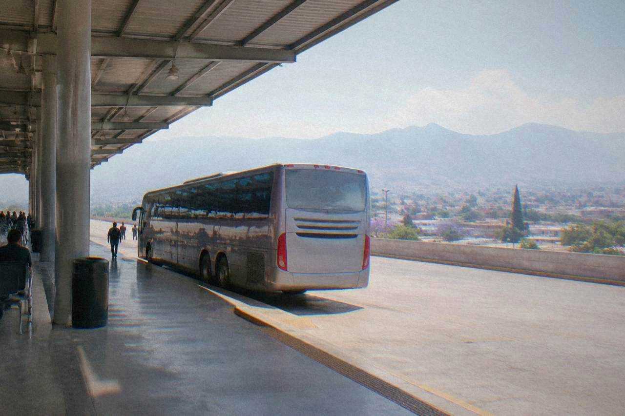 A long-distance bus parked at a terminal platform in Oaxaca City with mountains in the distance