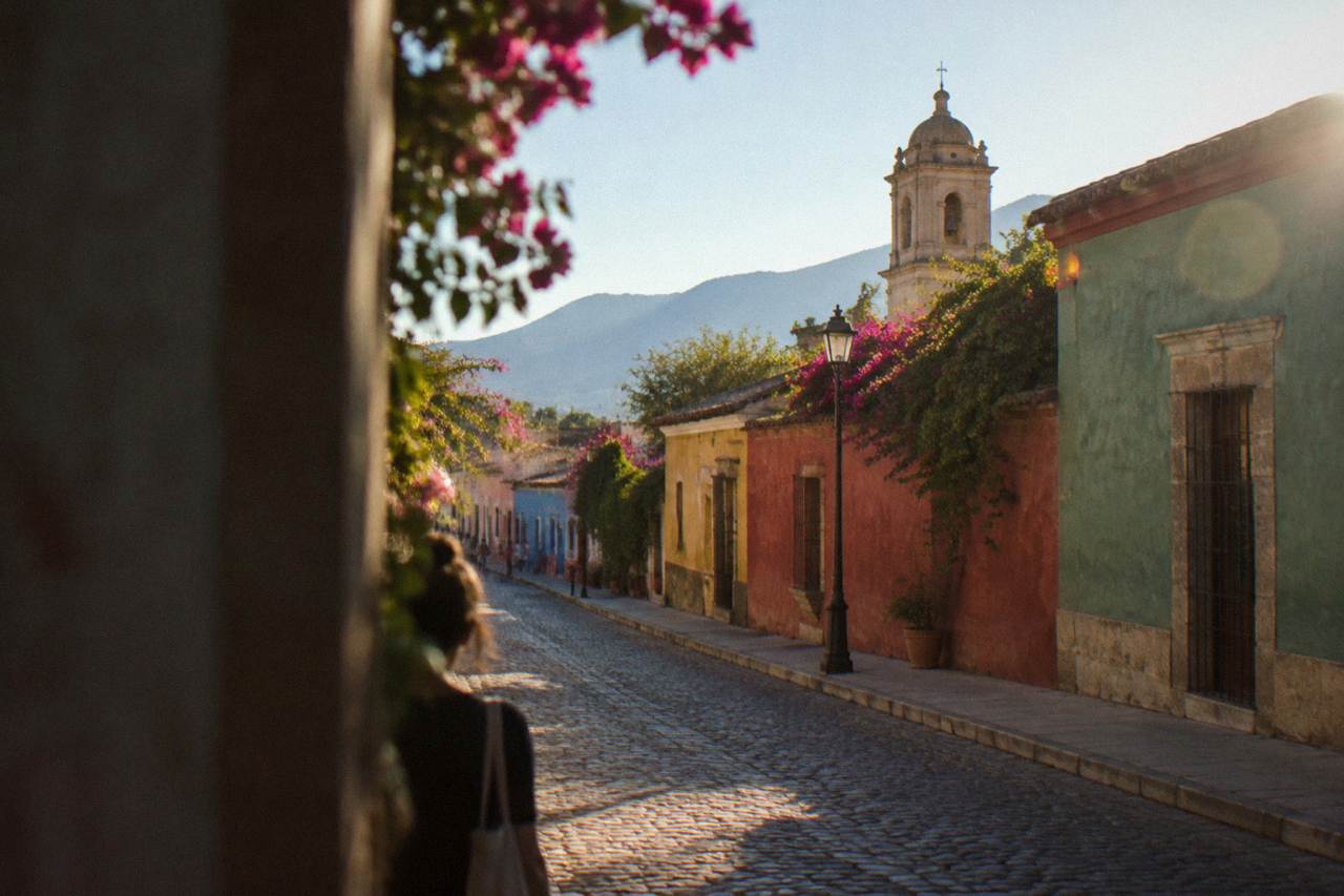 A quiet colonial street in Oaxaca City with green and red painted facades under a sunny sky