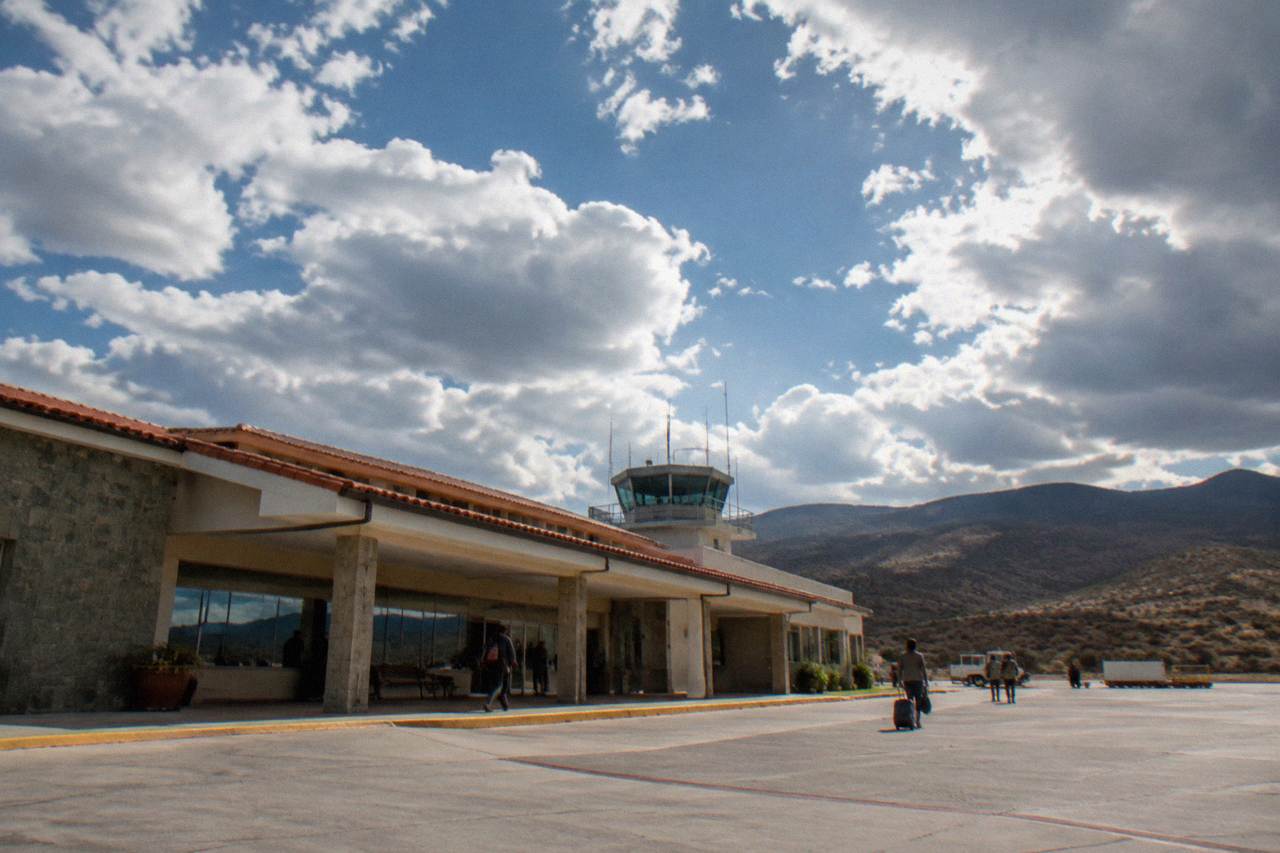 A small regional airport terminal building under a wide highland sky with hills behind it