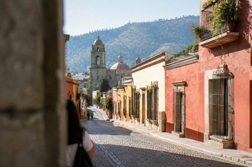 A rooftop view over the tiled roofs and church towers of Oaxaca City's historic centre at golden hour