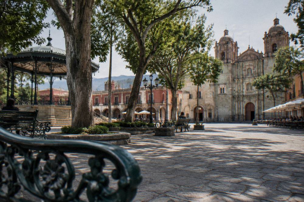 The Zócalo of Oaxaca City seen from a corner, with trees, benches and the cathedral facade behind