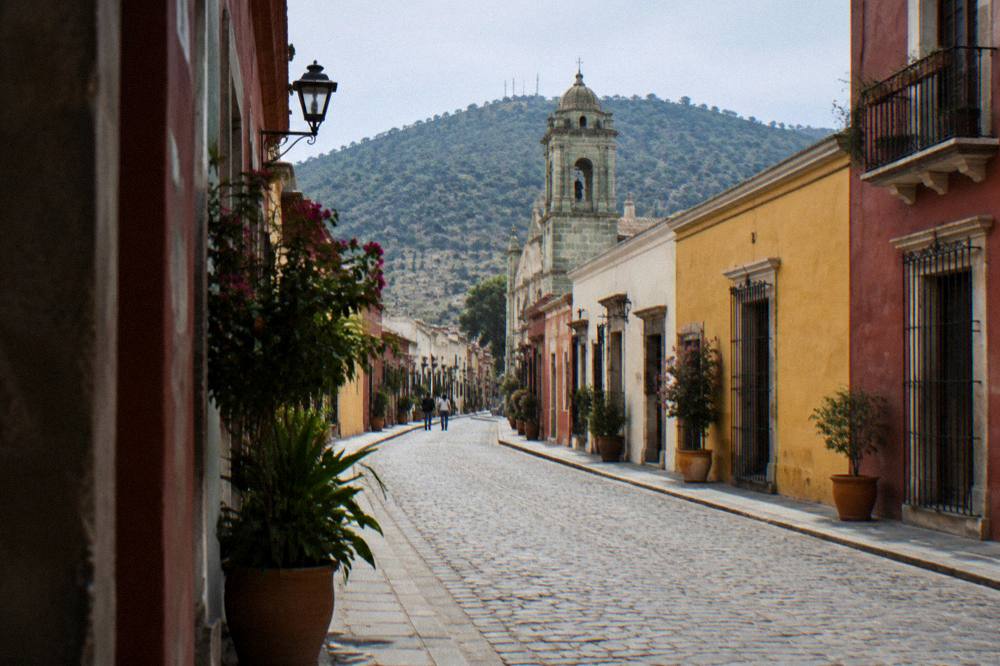 A narrow barrio street in Oaxaca with colourfully painted low houses and potted plants