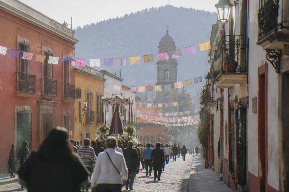 An evening procession moving through a decorated street in Oaxaca City with paper flags strung overhead