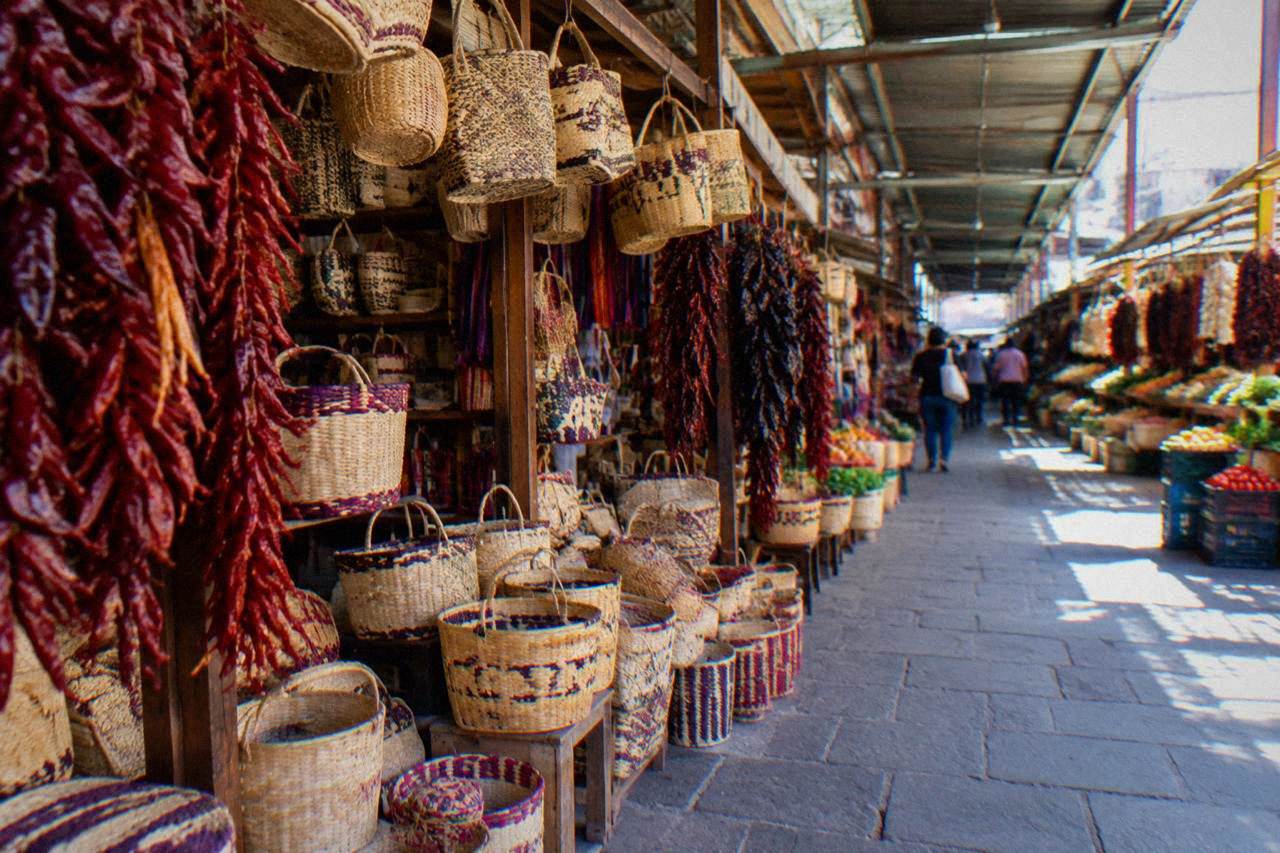 Market stalls with hanging woven baskets and chillies along a covered walkway in Oaxaca City