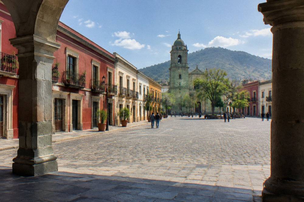The wide main square of Oaxaca City seen from a shaded arcade