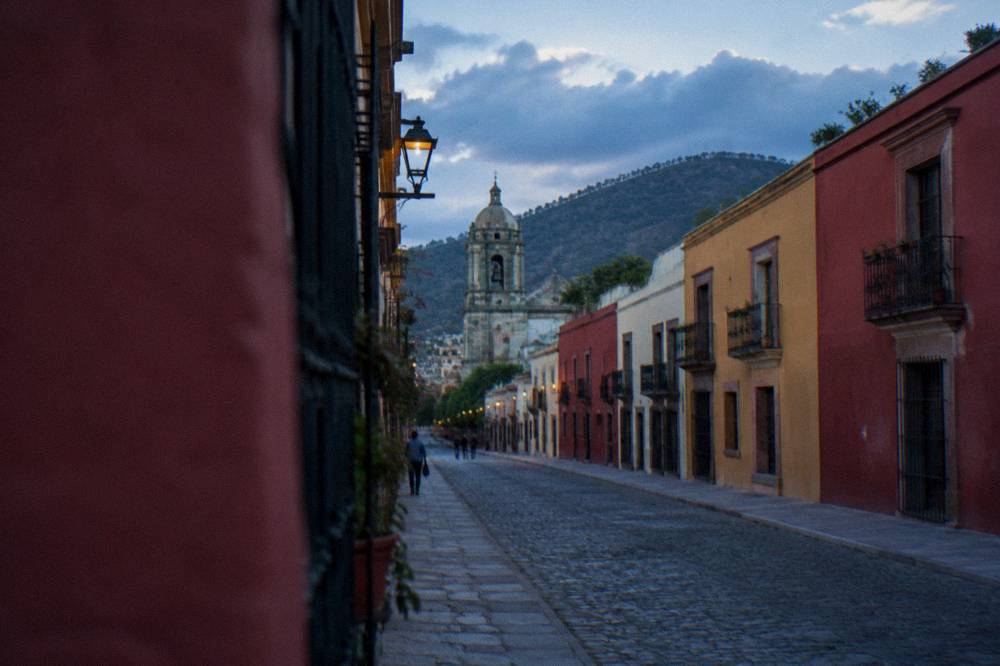 An afternoon sky over rooftops in Oaxaca City with clouds building over the hills