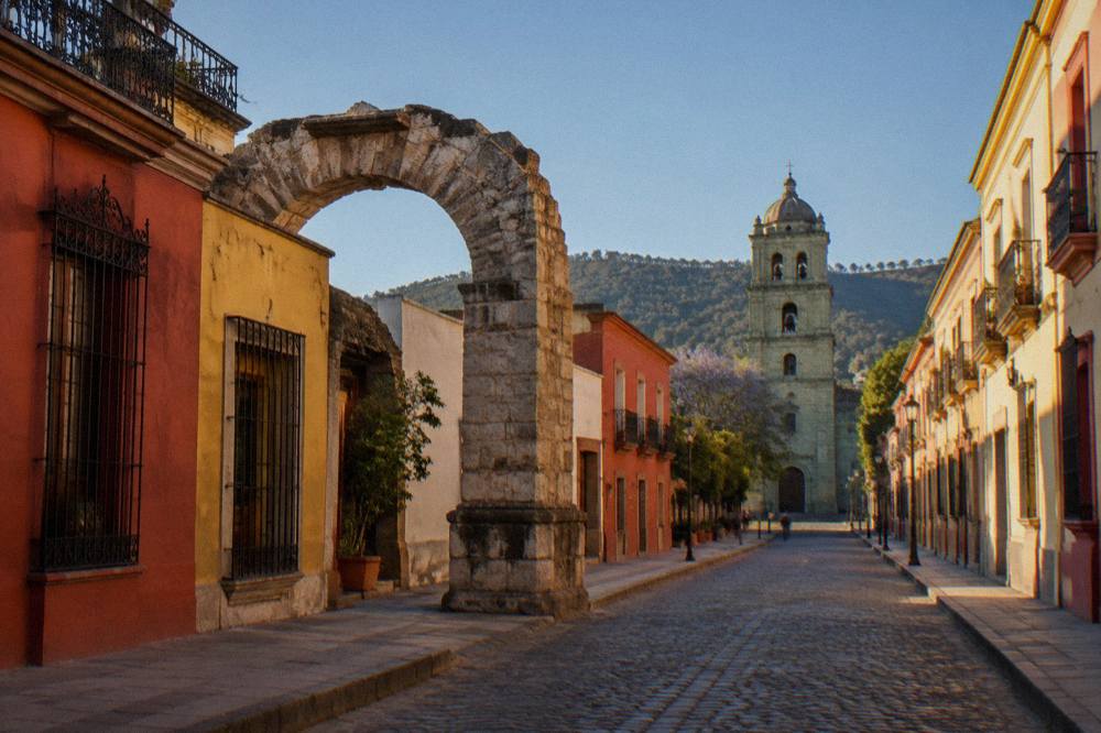 An old stone aqueduct arch standing among houses in a Oaxaca City street