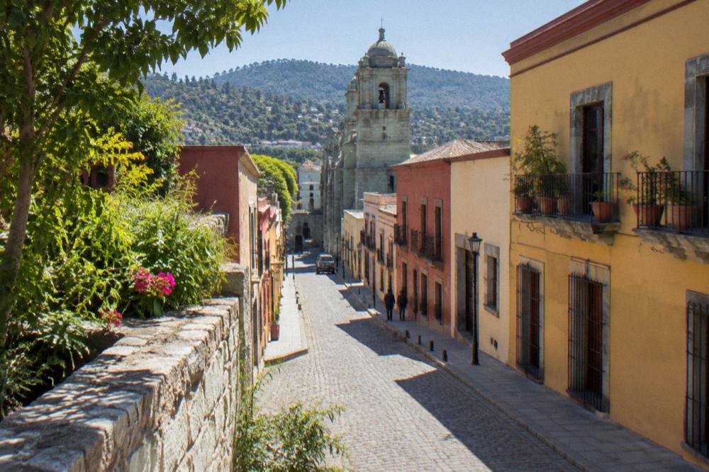 A sunlit corner with a stone wall and green plants in a Oaxaca City street