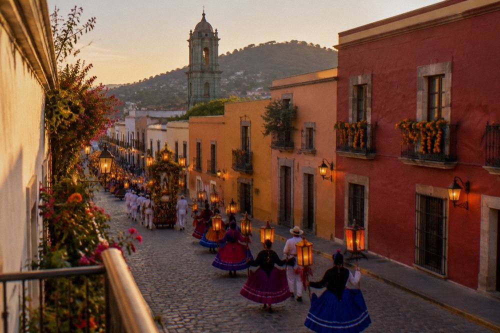 An evening street procession with dancers and lanterns moving through a decorated Oaxaca street
