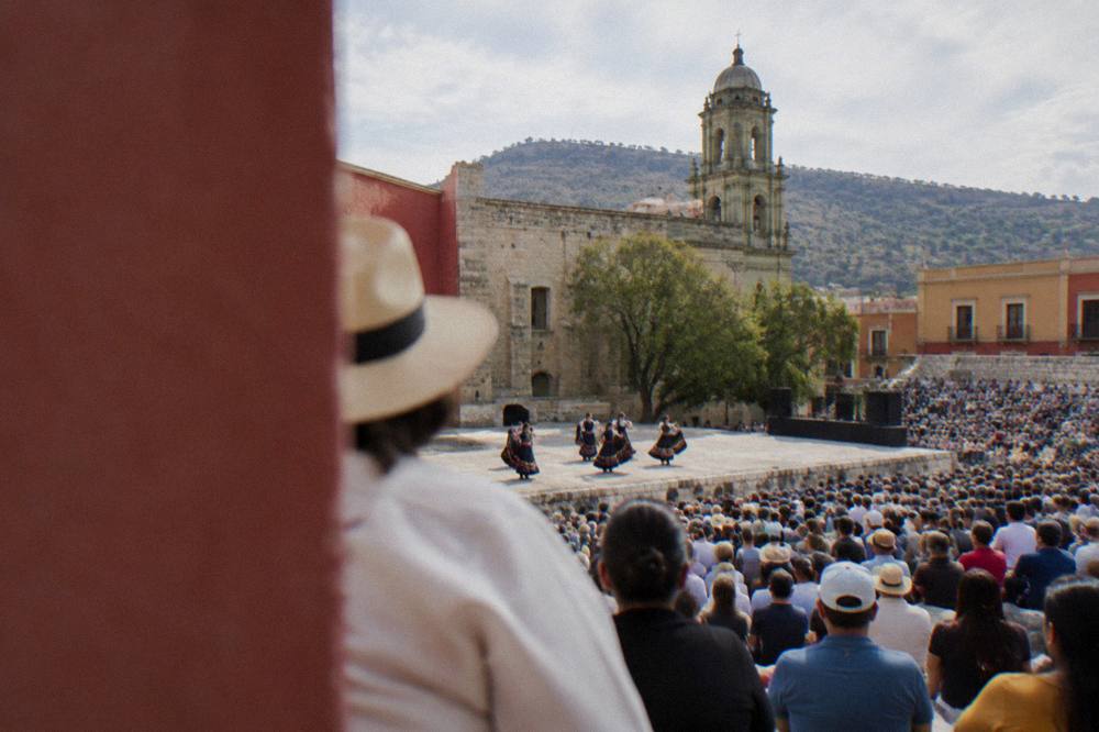 Festival crowds filling tiered stone seating at an outdoor auditorium in Oaxaca during a daytime performance