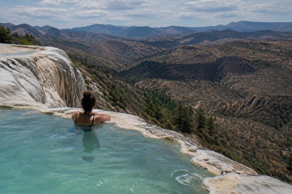 A swimmer resting at the edge of a rock pool overlooking the wide valley below Hierve el Agua