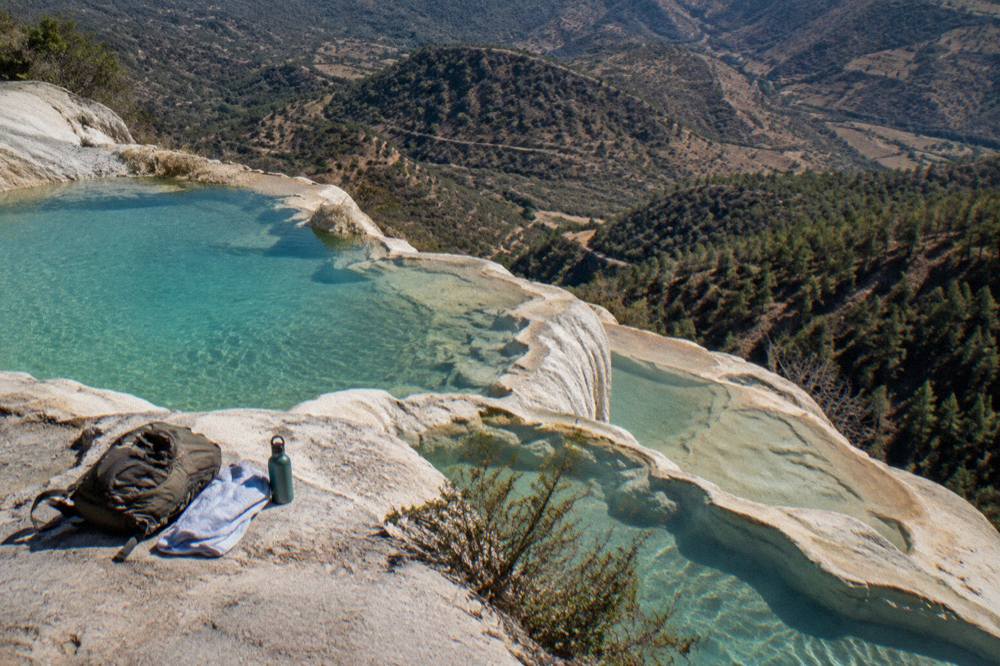 A day pack, towel and water bottle on a rock ledge beside the turquoise pools