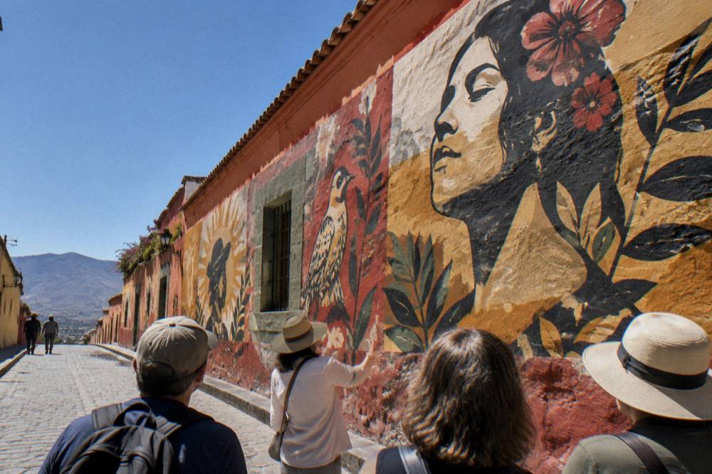 A small group of visitors listening to a guide in front of a mural