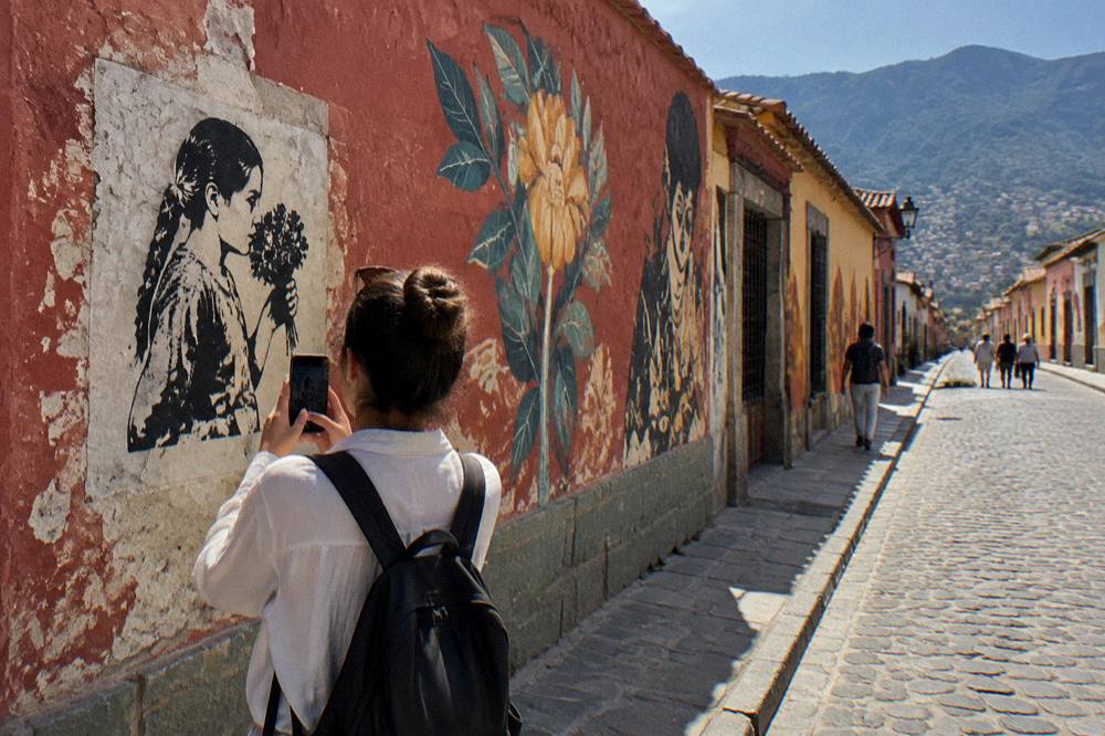 A visitor photographing a stencil pasted on a wall in Oaxaca City
