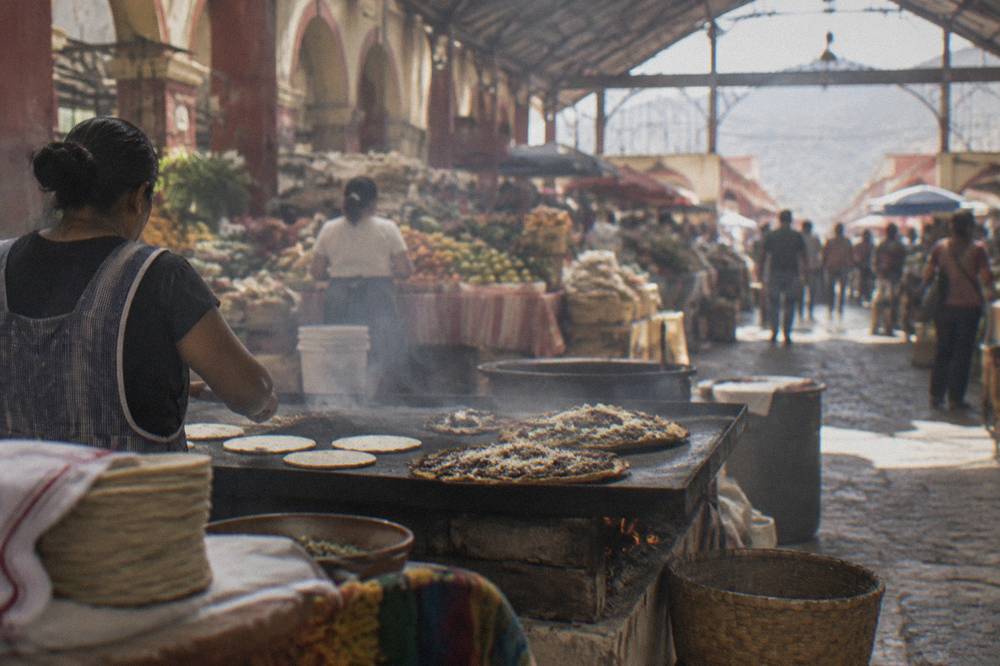 Griddle with tlayudas and tortillas cooking over open heat in a market food stall
