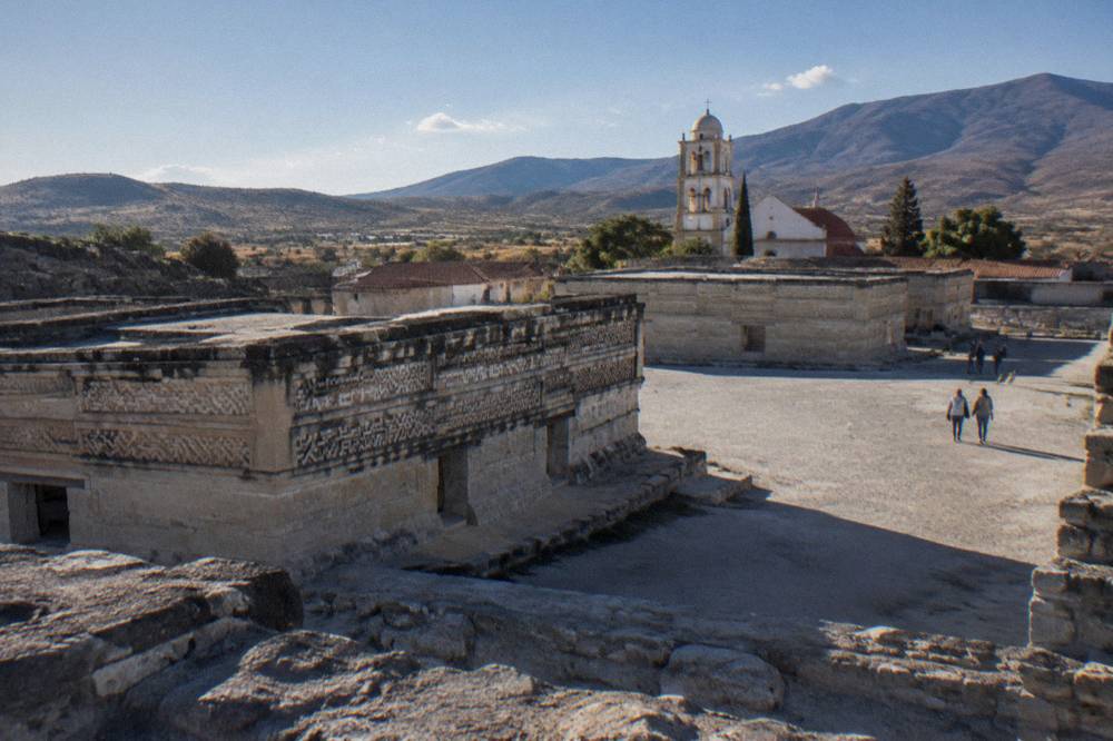 Wide view over low ancient stone structures with a church tower behind them