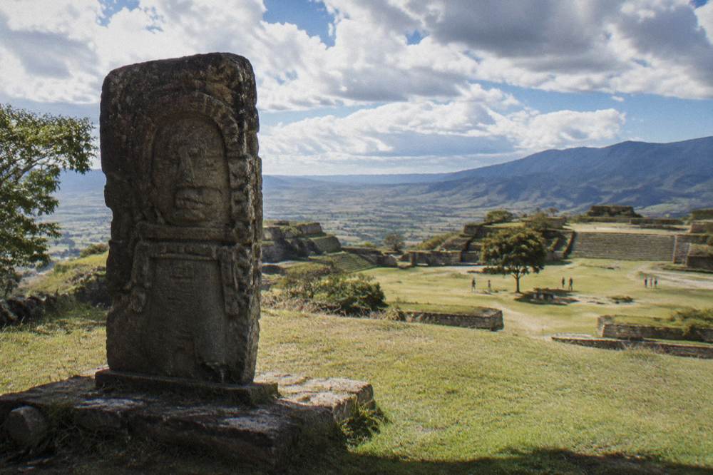 Carved stone monument standing on a grassy terrace of an archaeological site