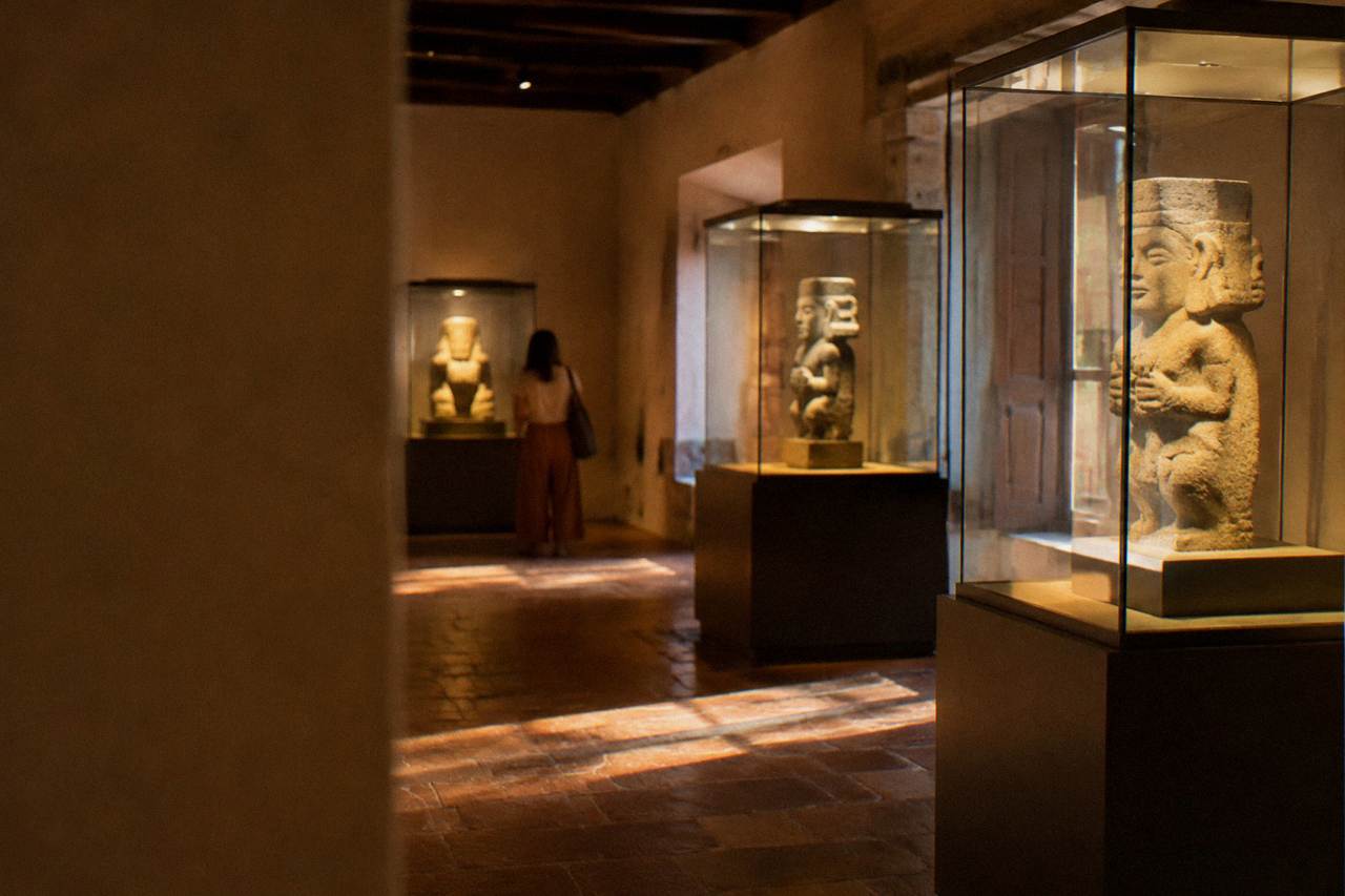 A museum gallery in Oaxaca City with pre-Hispanic stone figures displayed in illuminated cases