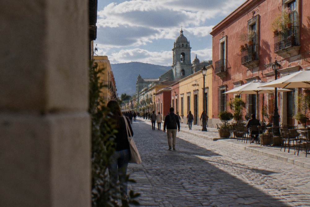A pedestrian street in Oaxaca with people walking past colonial facades in late afternoon light