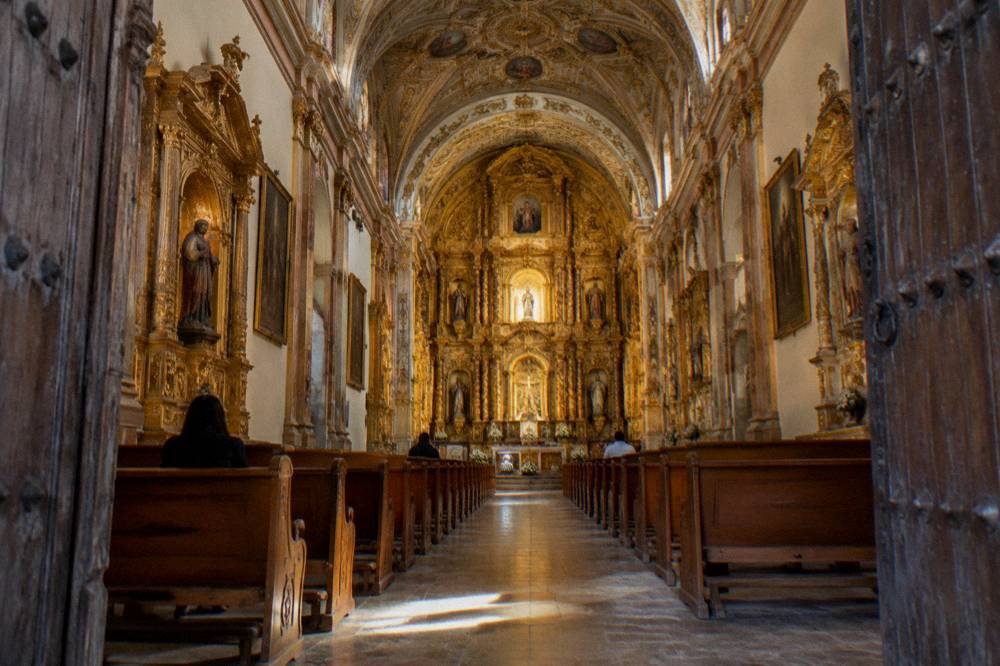 The ornate gilded interior of a church nave in Oaxaca seen from the entrance