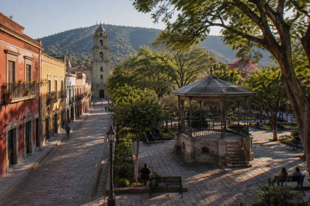A shaded park square in Oaxaca with trees, benches and a stone bandstand