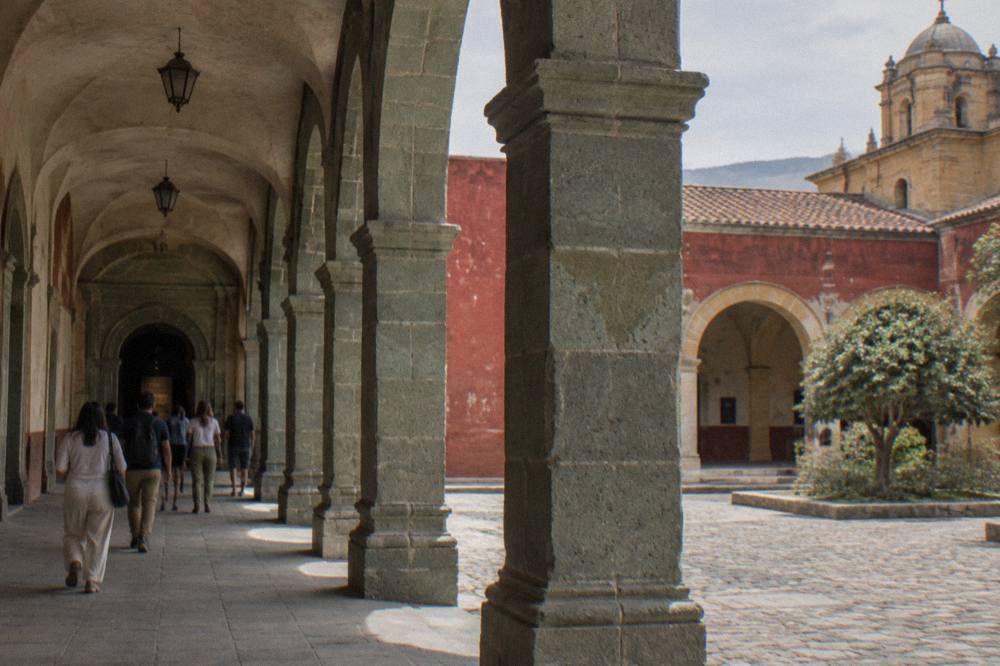 Visitors walking through a stone arcade of the former convent toward a museum entrance in Oaxaca City