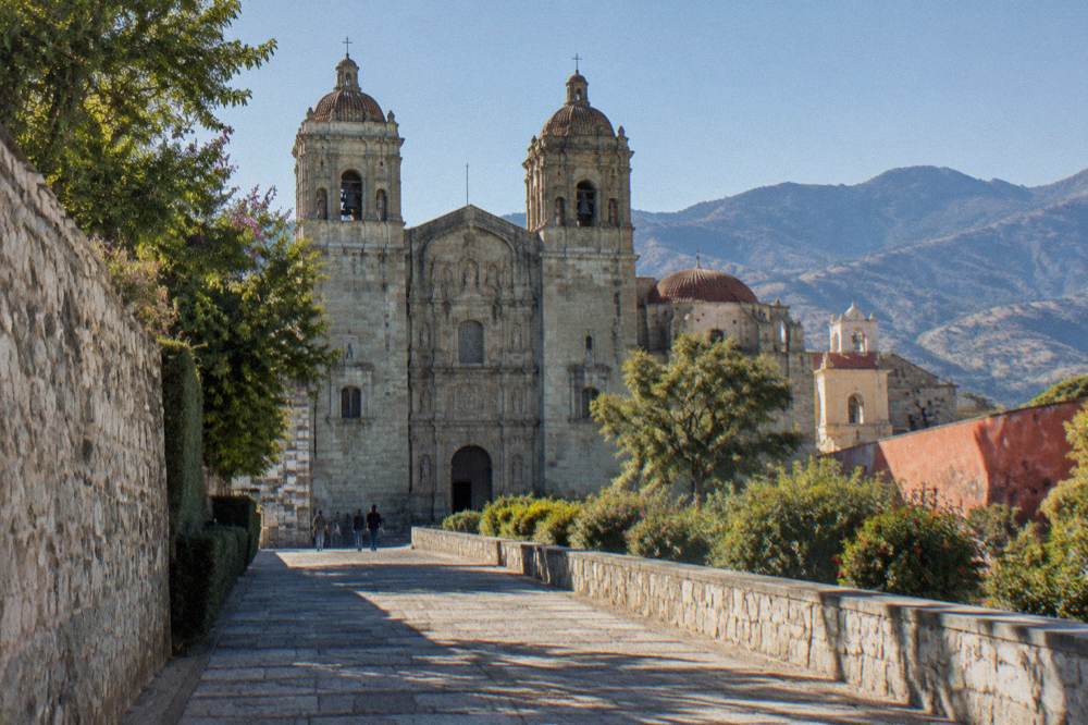 A wide walkway lined with old stone walls and greenery leading through the Santo Domingo complex in Oaxaca City