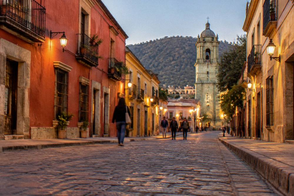 An evening street in Oaxaca City with warm lights on colonial facades and people walking