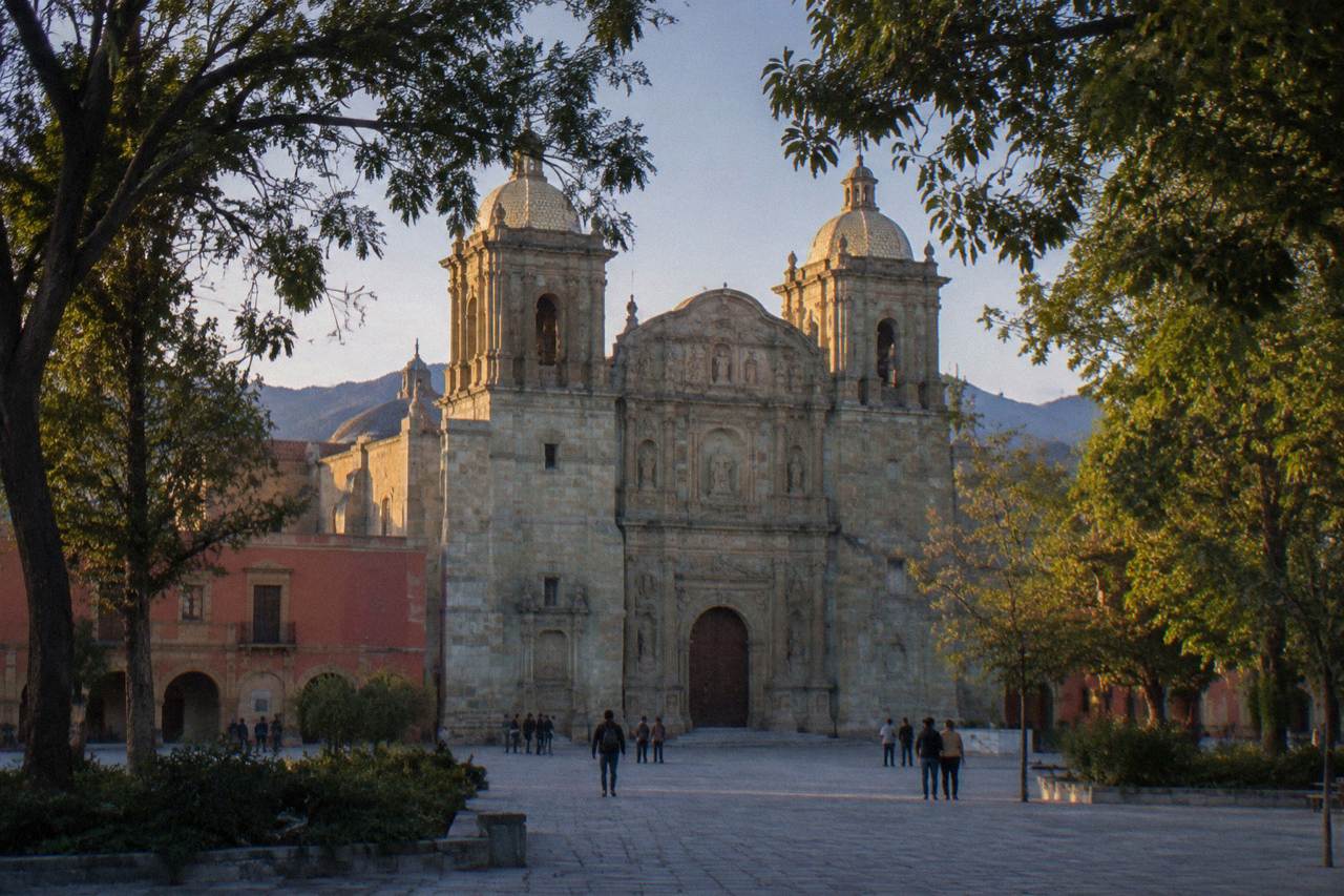 The stone facade of the Oaxaca cathedral standing at the edge of a wide city square in warm afternoon light