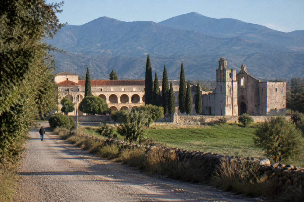 Gravel road leading toward a stone convent complex with cypress trees
