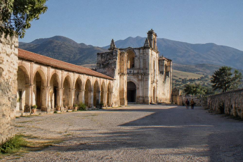 A wide gravel esplanade with monastery walls on two sides and hills beyond