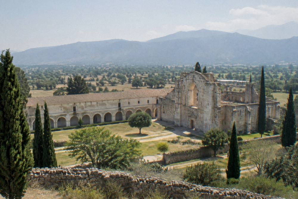 A low stone wall and cypress trees framing hills under a wide sky