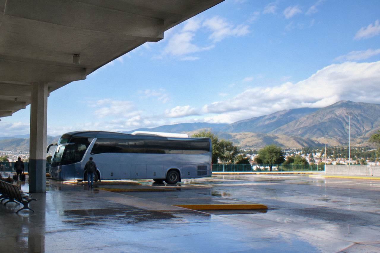 A long distance bus parked at a terminal in a Mexican city with mountains behind it