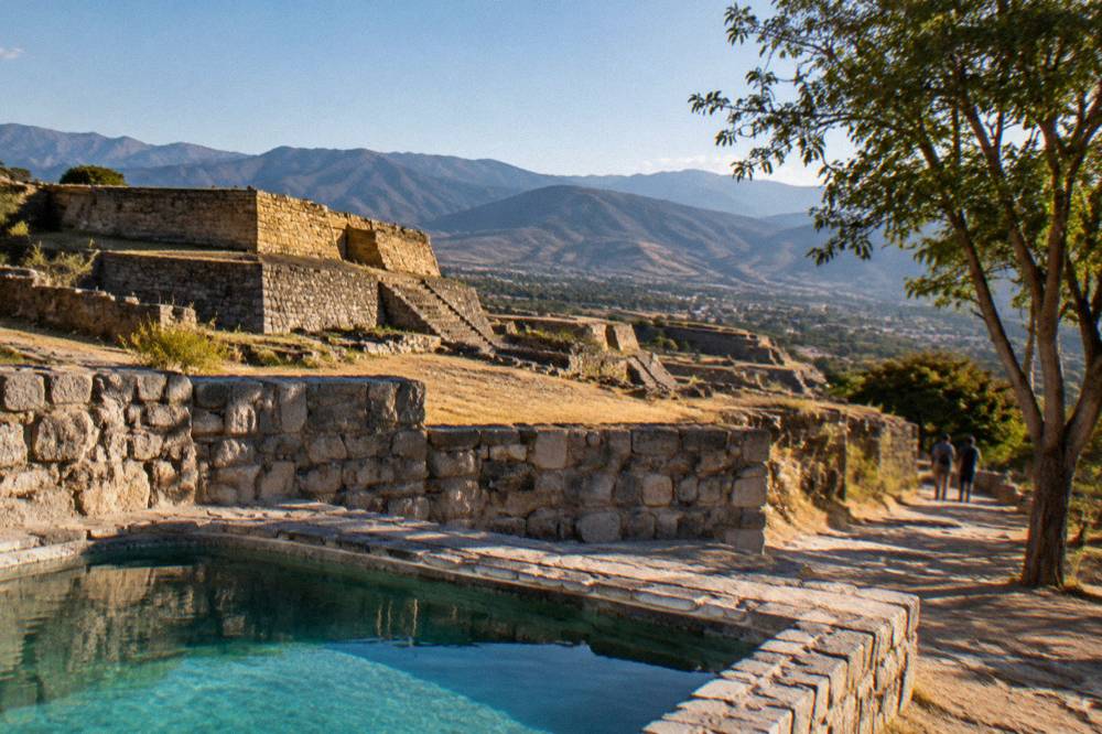Stone ruins of an archaeological site on a hillside above a valley in Oaxaca