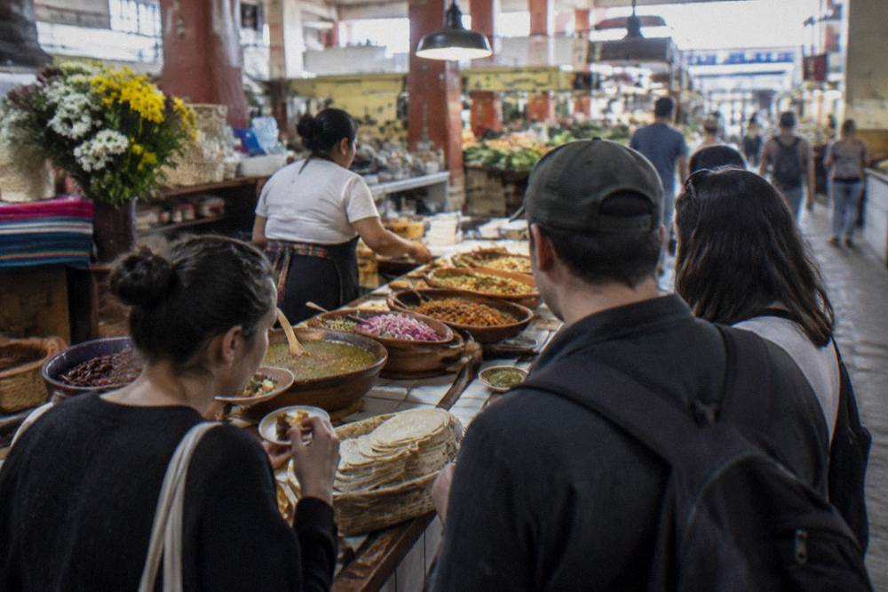 Visitors tasting food at a busy indoor market stall in Oaxaca